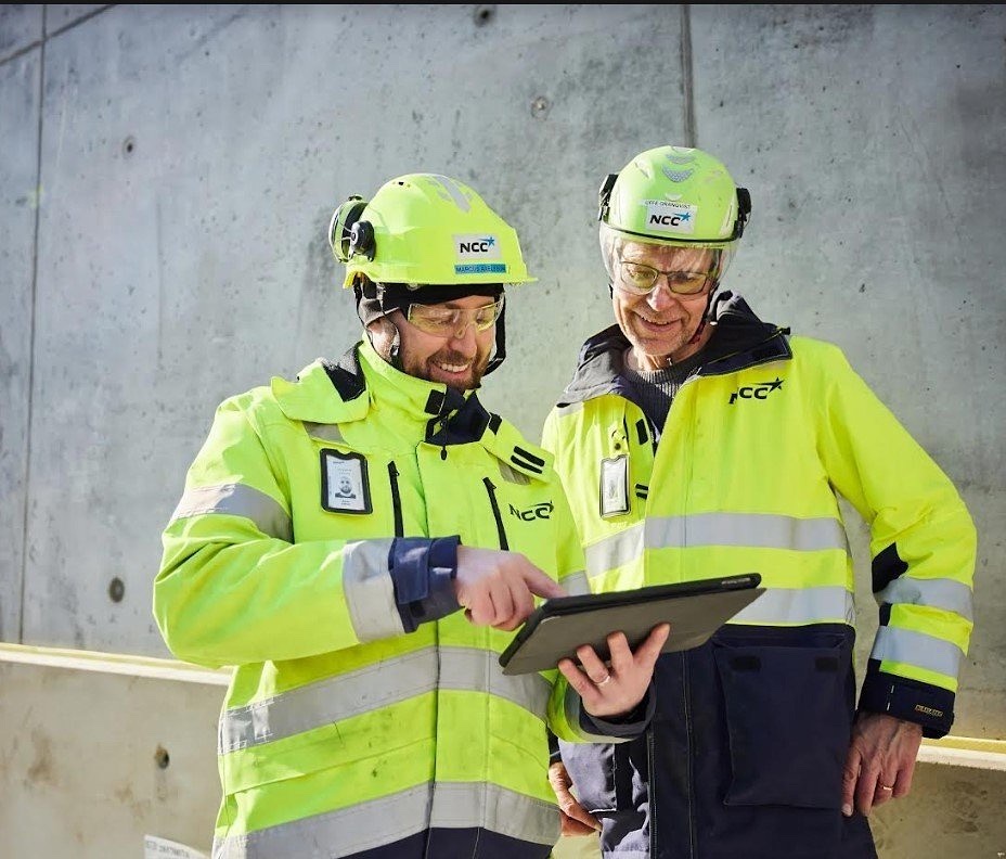 To medarbejdere fra NCC i sikkerhedsudstyr kigger på en tablet
